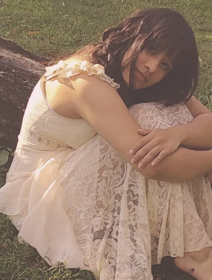 María Andrea abraza sus rodillas junto a un árbol