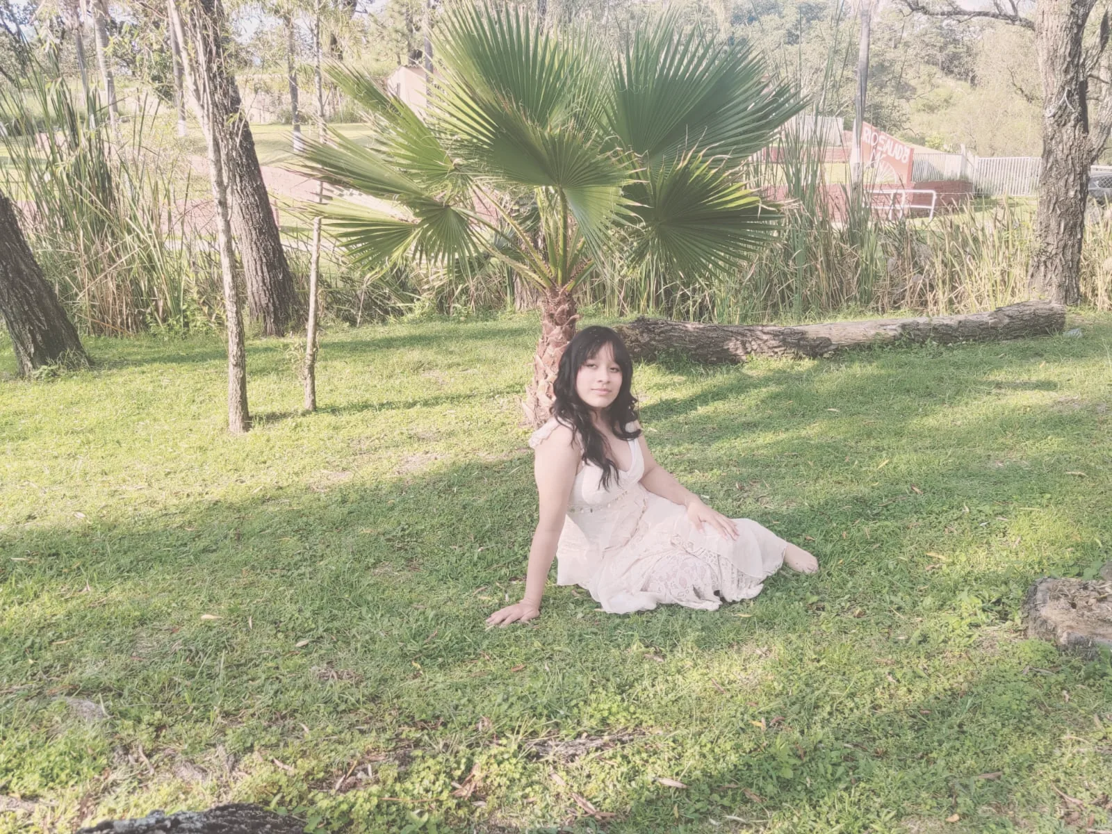 María Andrea sentada en el pasto bajo una palmera